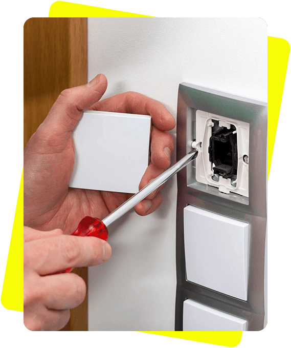 A person using a screwdriver to install a white switch plate on a wall.
